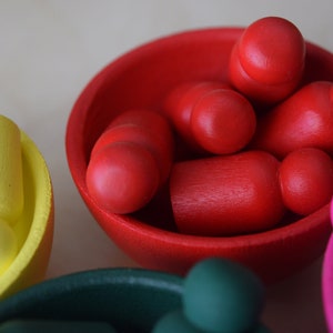 Puede incluir: Un conjunto de cuencos de madera llenos de bolas de madera de colores. Los cuencos son rojo, verde, amarillo y rosa. Las bolas son de diferentes tamaños y formas.