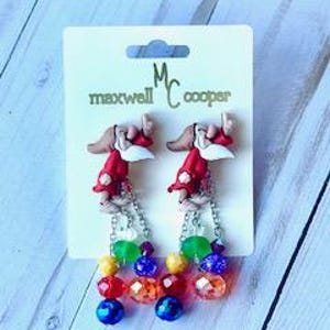 May include: A pair of dangle earrings featuring a red and white cartoon character with a white beard and a red hat. The earrings have a rainbow of colorful beads and a silver chain.