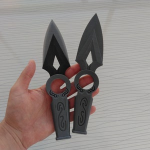 May include: Two gray, plastic throwing knives with a diamond-shaped blade and a ring handle. The knives have intricate designs on the handle.