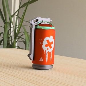 May include: A red and white grenade-shaped object with a green top and a white plus sign on the side. The object is on a wooden surface.