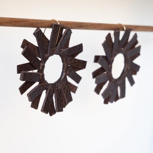 Angled shot of a dark brown espresso pair of circular windmill shaped leather earrings hanging from a small walnut wood rod