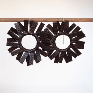 Pair of circular earrings hanging from a small walnut wood rod each made of dark brown espresso colored leather strips stitched together to create the look of a spinning windmill