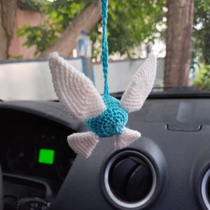 May include: A blue and white crocheted bird hanging from a rearview mirror in a car. The bird has white wings and a blue body.