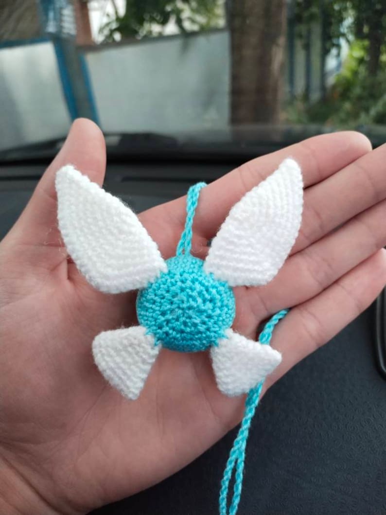 May include: A crocheted blue and white fairy charm with wings. The charm is attached to a blue cord.