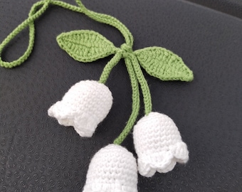 May include: A crocheted white and green lily of the valley flower charm with a long green cord.