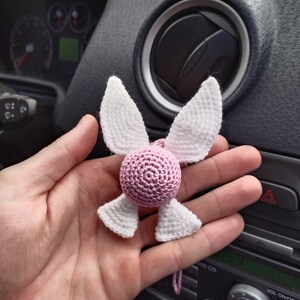 May include: A pink and white crocheted angel ornament with wings. The ornament is hanging from a string.