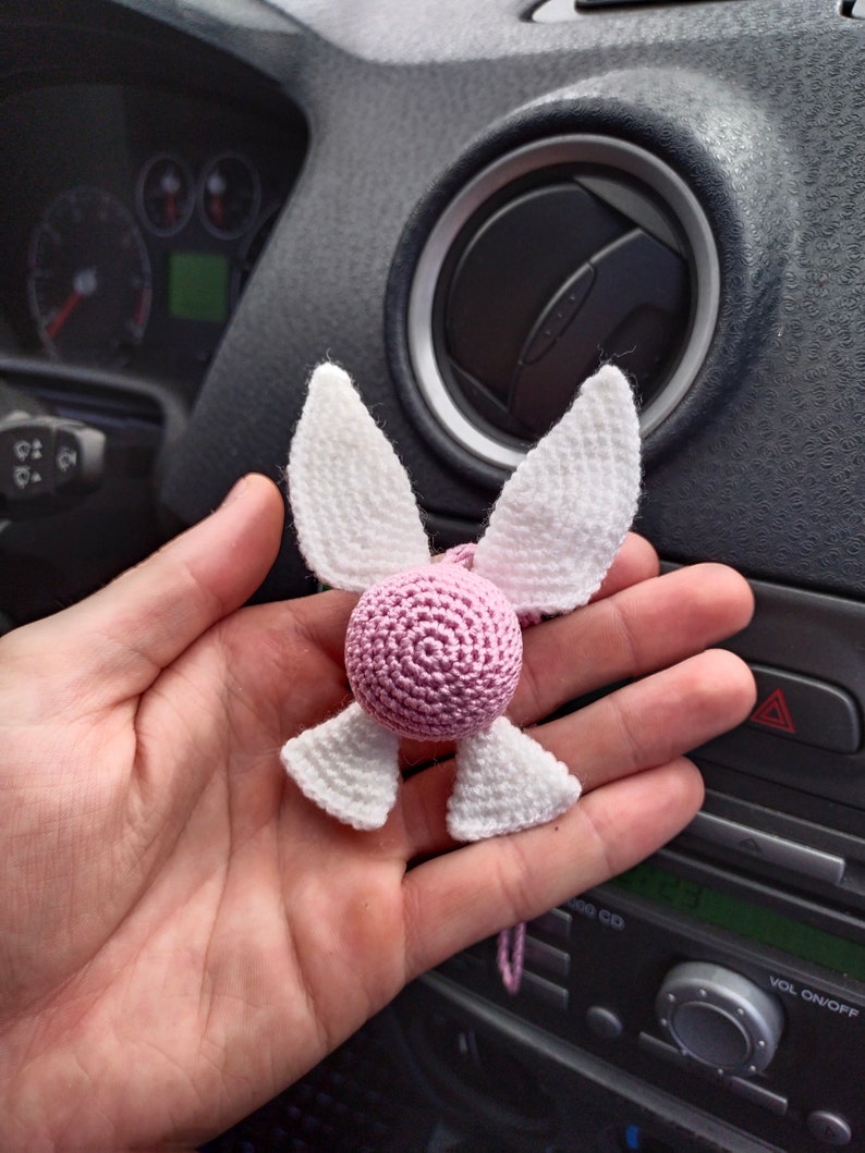 May include: A pink and white crocheted angel ornament with wings. The ornament is hanging from a string.