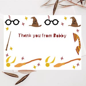 May include: A white thank you card with a Harry Potter theme. The card features a red and gold striped scarf, a black wand, a brown wizard hat, and a pair of glasses. The text on the card reads "Thank you from Bobby".