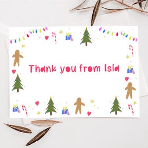 May include: A white card with a pink border and the text "Thank you from Isla" in pink. The card is decorated with colourful Christmas-themed illustrations, including gingerbread people, Christmas trees, candy canes, and presents.