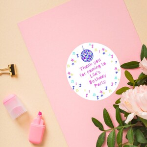 May include: Round white thank you sticker with a purple disco ball, pink stars, and blue musical notes. The text reads "Thank you for coming to Lila's Birthday Party".