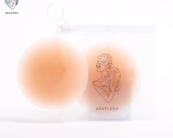 Puede incluir: Dos almohadillas adhesivas de silicona de color carne en una bolsa de plástico transparente con el nombre de la marca "ARAFLESH" impreso en la bolsa.