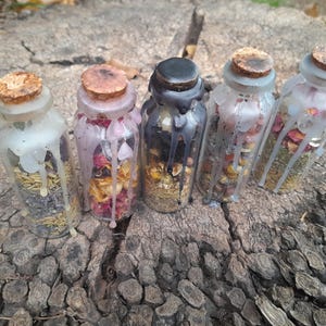 May include: Five small glass jars with cork lids filled with dried herbs and flowers. The jars are sealed with wax and have a rustic, vintage aesthetic.