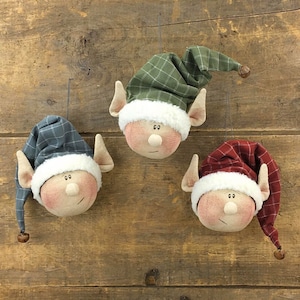 May include: Three handmade elf ornaments with plaid fabric hats and white fur trim. The elves have painted faces and are hanging from a string.