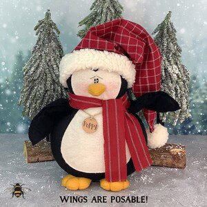 May include: A plush penguin wearing a red and white plaid hat and a red and white striped scarf. The penguin has a name tag that says "Poppy".