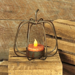 May include: A rustic metal pumpkin candle holder with a tealight candle inside. The candle holder is made of wire and has a distressed finish.