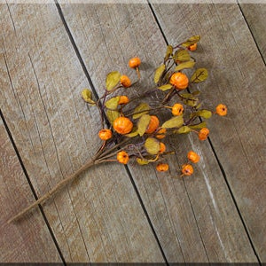 May include: A branch of faux fall foliage with small orange berries and green leaves. The branch is lying on a wooden surface.