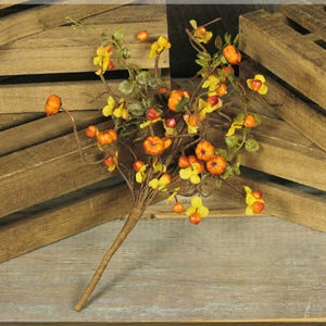 May include: A fall-themed decorative stem featuring small orange pumpkins, yellow flowers, and green leaves. The stem is brown and has a natural, rustic appearance. The arrangement is set against a backdrop of wooden planks.
