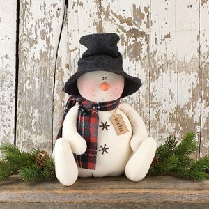 Könnte beinhalten: Ein weißer Schneemann mit einem schwarz-rot karierten Schal, einem schwarzen Hut und einem braunen Etikett mit der Aufschrift "Winter".