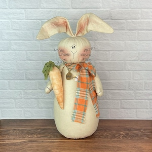 May include: A white bunny rabbit doll with a carrot in its hand. The bunny is wearing a plaid scarf and a tag that says "Reno".