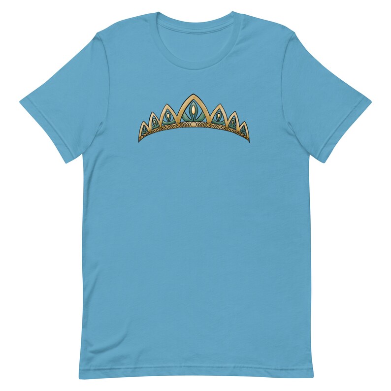 May include: A light blue t-shirt with a gold and green crown design. The crown has five points and is decorated with small, round, blue gems.