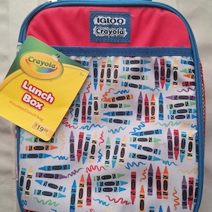 May include: An insulated Crayola lunch box with a red top and blue trim. The main body of the bag is white with a colorful crayon pattern. The bag has a handle and a tag that reads "Lunch Box".