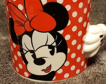 May include: A red and white ceramic mug with a 3D Minnie Mouse handle. The mug features a cartoon image of Minnie Mouse with a red bow and white polka dots.