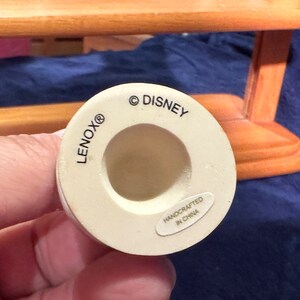 May include: White ceramic figurine base with the text "LENOX&reg;" and "&copy; DISNEY" printed on the side. The base also has a smaller label that reads "HANDCRAFTED IN CHINA".