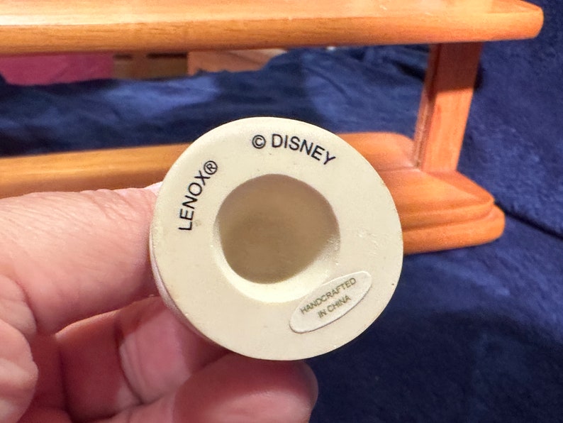 May include: White ceramic figurine base with the text "LENOX&reg;" and "&copy; DISNEY" printed on the side. The base also has a smaller label that reads "HANDCRAFTED IN CHINA".