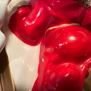 Peut inclure: Une figurine en c&eacute;ramique d'une personne portant une robe rouge. La figurine est peinte avec une finition brillante et a un fond blanc.