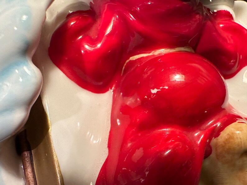 Peut inclure: Une figurine en c&eacute;ramique d'une personne portant une robe rouge. La figurine est peinte avec une finition brillante et a un fond blanc.