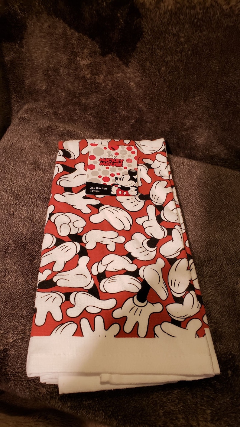 May include: Two red and white kitchen towels featuring a Mickey Mouse design. The towels have a repeating pattern of Mickey Mouse's white gloved hands on a red background. The tag on the towel reads "Disney Mickey Mouse 2pk Kitchen Towels".