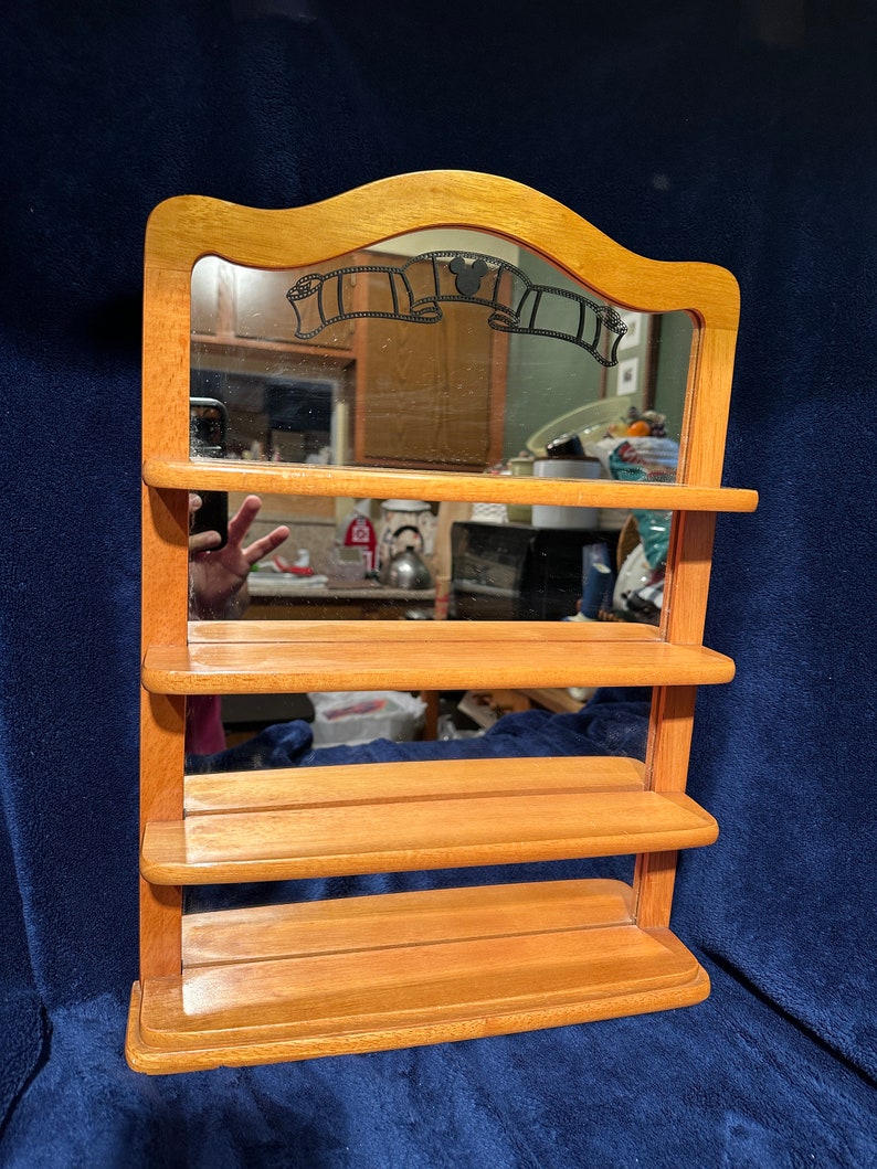 May include: Wooden shelf unit with a mirror and four shelves. The mirror has a Mickey Mouse silhouette and film reel design.