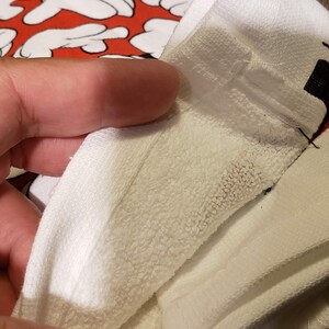 May include: Close-up of a white towel with a red and black Mickey Mouse design. The towel is folded in half and the seam is visible.