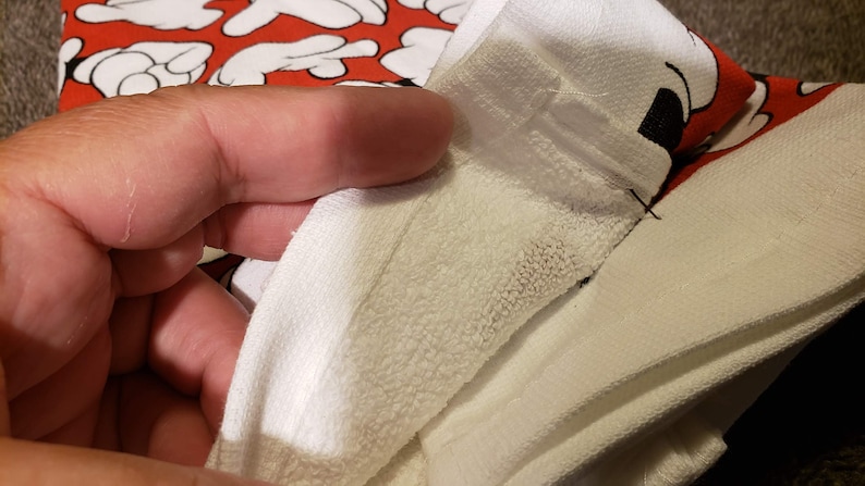 May include: Close-up of a white towel with a red and black Mickey Mouse design. The towel is folded in half and the seam is visible.