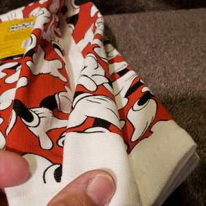 May include: A folded white and red kitchen towel with a Mickey Mouse hand print pattern. The towel has a yellow tag with the text "Mickey Mouse" on it.