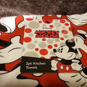 May include: Two red and white kitchen towels featuring a Mickey Mouse design. The towels show Mickey Mouse's white gloves and red shorts. The label reads "Disney Mickey Mouse 2pk Kitchen Towels".