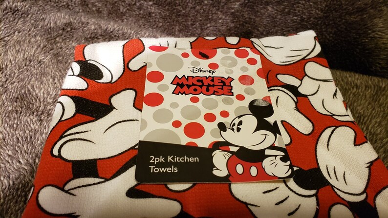 May include: Two red and white kitchen towels featuring a Mickey Mouse design. The towels show Mickey Mouse's white gloves and red shorts. The label reads "Disney Mickey Mouse 2pk Kitchen Towels".