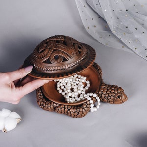 Może przedstawiać: Brązowa ceramiczna szkatułka w kształcie żółwia z rzeźbioną pokrywką, otwartą, aby ukazać naszyjnik z pereł w środku.