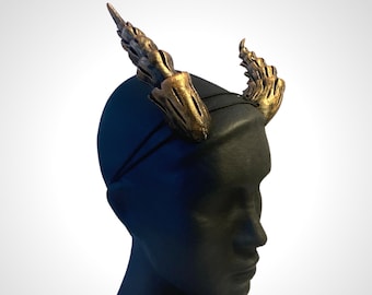 May include: A black headband with two gold horns attached. The horns are detailed with a textured, scaly design.