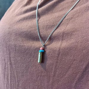 May include: A silver chain necklace with a gold bullet casing pendant and three small beads: one pink, one blue, and one turquoise.