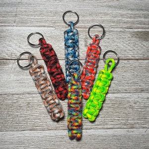 May include: Six colorful paracord keychains with metal key rings. The keychains are made of braided paracord in various colors, including red, blue, green, orange, and black.