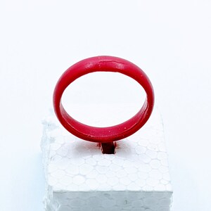 May include: A bright red silicone ring on a white foam display stand.