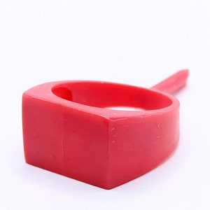 May include: A bright red plastic ring with a square-shaped band and a pointed top.