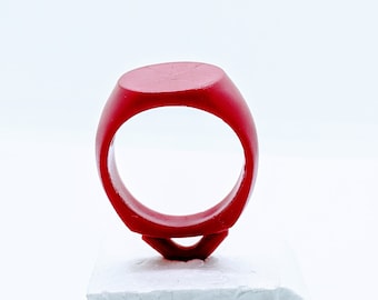 May include: A red ring with a flat top, sitting on a white platform.