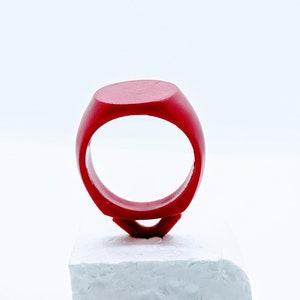 May include: A red ring with a flat top, sitting on a white platform.