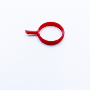 May include: A red plastic ring with a small handle attached to it.