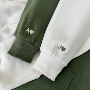 May include: Two hooded sweatshirts with embroidered hearts and initials, one in olive green and one in white.