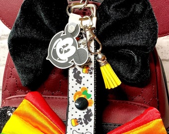 Puede incluir: Una mochila de Minnie Mouse de imitación de cuero rojo con orejas negras y un lazo de terciopelo negro. Un lazo a rayas arcoíris está unido a una diadema negra con lentejuelas negras. Una cinta blanca con lunares negros e imágenes de temática de Halloween está unida a la mochila con un amuleto de Mickey Mouse.