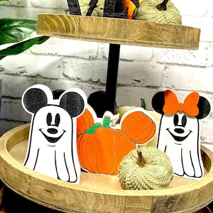 May include: A two-tier wooden tiered tray decorated with Halloween-themed decorations. The top tier features a black wooden "LOVE" sign with a pumpkin-shaped Mickey Mouse head. The bottom tier features two ghost-shaped Mickey Mouse and Minnie Mouse figures with pumpkins and gourds.