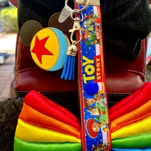 May include: A red backpack with black ears and a rainbow bow. A blue and white Toy Story lanyard with a blue tassel hangs from the backpack.
